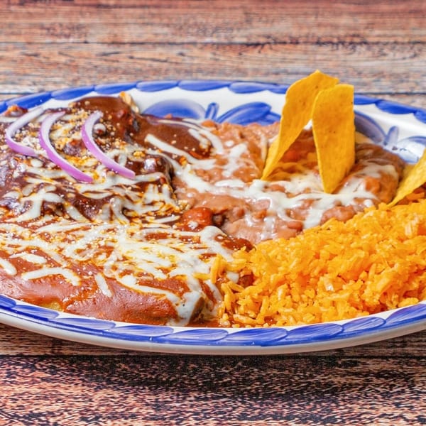 A plate of enchiladas with mole sauce, refried beans, rice, and tortilla chips.
