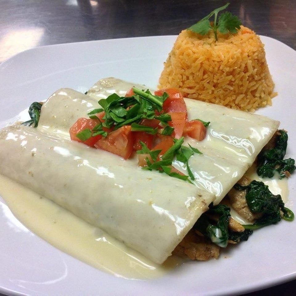 Three enchiladas covered in white sauce, topped with diced tomatoes and cilantro, served with rice.