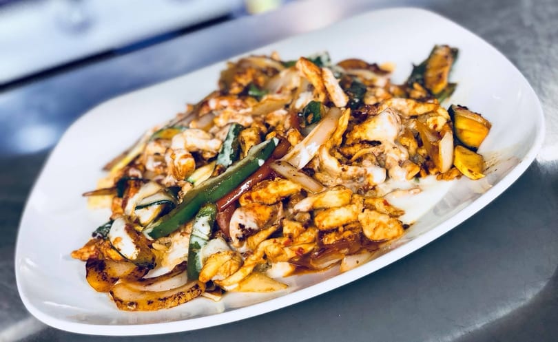 Chicken fajitas with grilled onions, green peppers, and zucchini on a white plate.