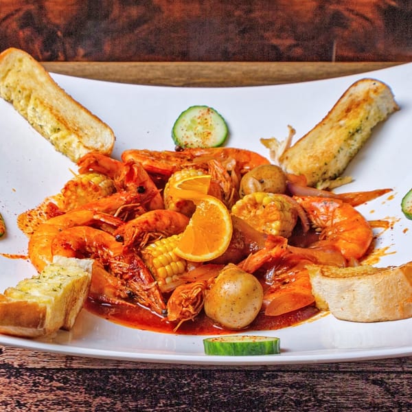 Shrimp boil with corn, potatoes, onions, and orange slices, served with garlic bread on a white plate.