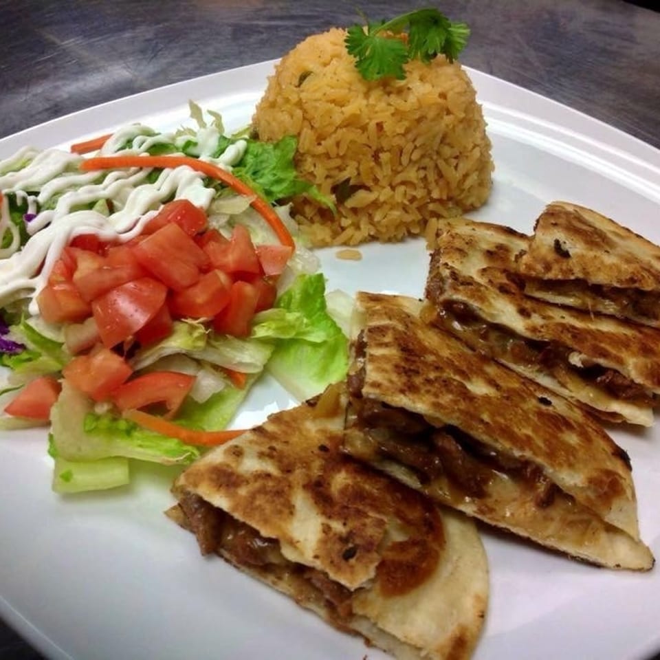 Quesadillas with rice and a side salad with tomatoes and dressing on a white plate.